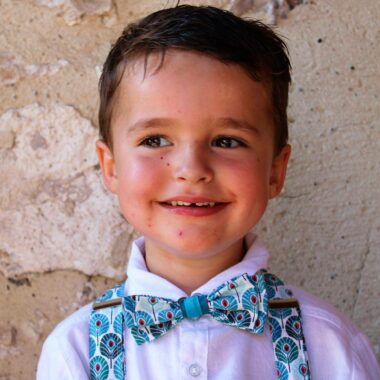 ensemble noeud papillon et bretelles à motifs plume de paon bleues portés par un petit garçon sourillant