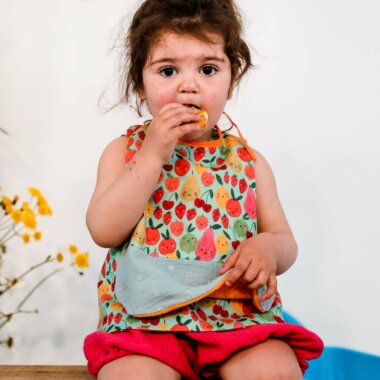 fillette avec un bavoir coloré et imprimé fruits en train de manger pour un repas tout en gardant ses vetements bien propres