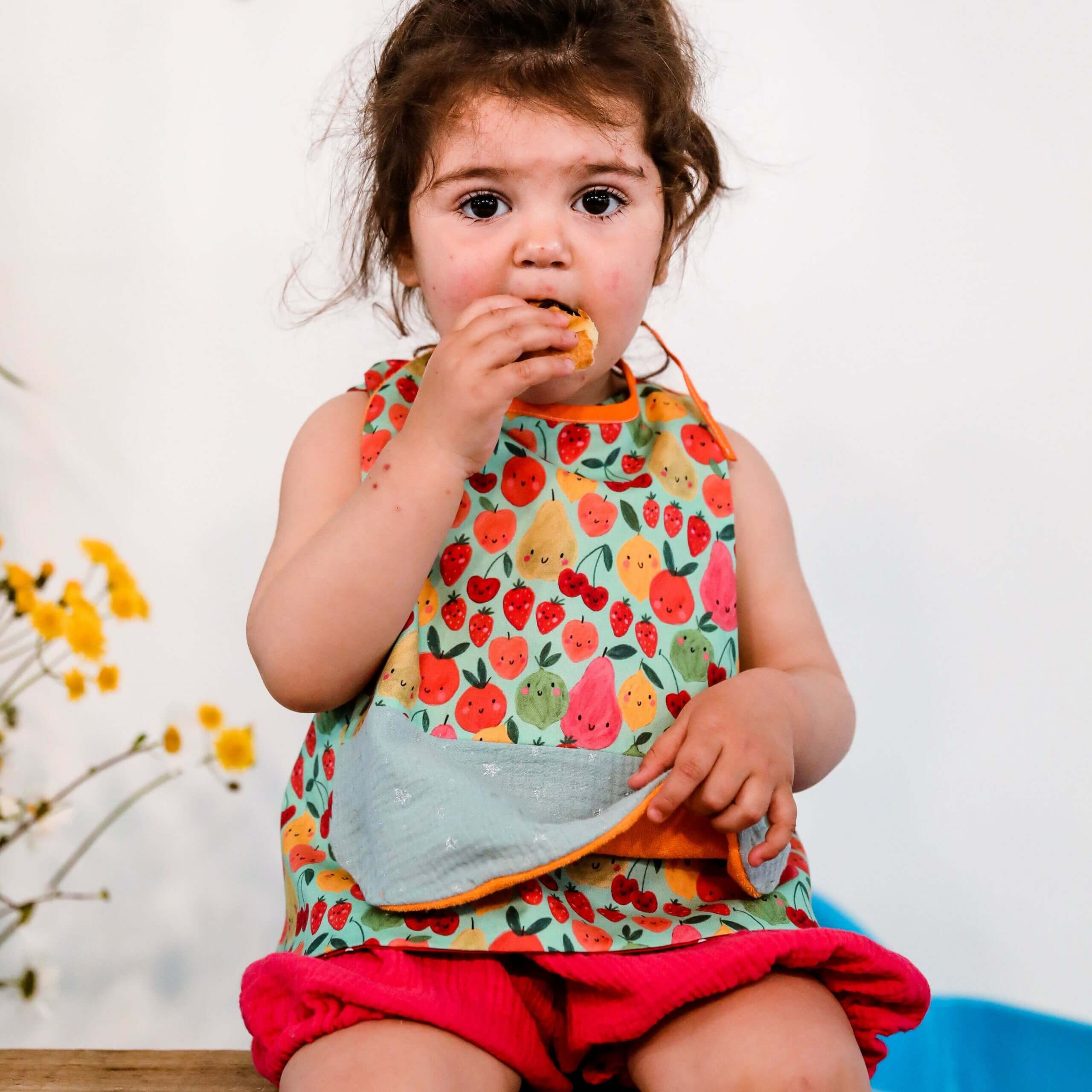 fillette avec un bavoir coloré et imprimé fruits en train de manger pour un repas tout en gardant ses vetements bien propres